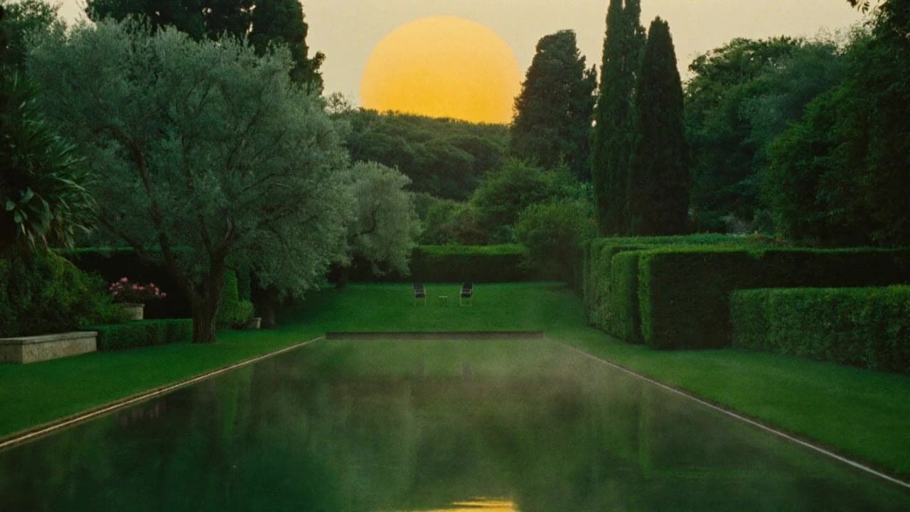 A garden at golden hour: an enormous sun resting on a green horizon, mirrored in a still reflecting pool, with two chairs facing each other on the lawn between cypress and olive trees.